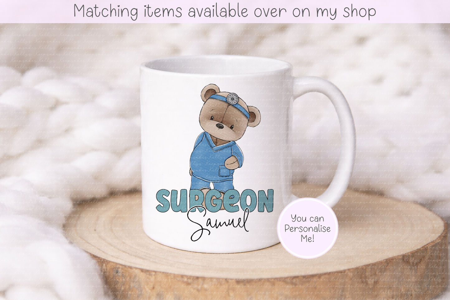 A white ceramic mug featuring a cartoon teddy bear dressed as a surgeon with the text 'SURGEON Samuel' printed on it. The mug is displayed on a round wooden slice with a soft, fuzzy white blanket background.